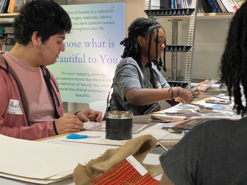 3 people sitting at a table and working with various documents and crafts supplies in front of them